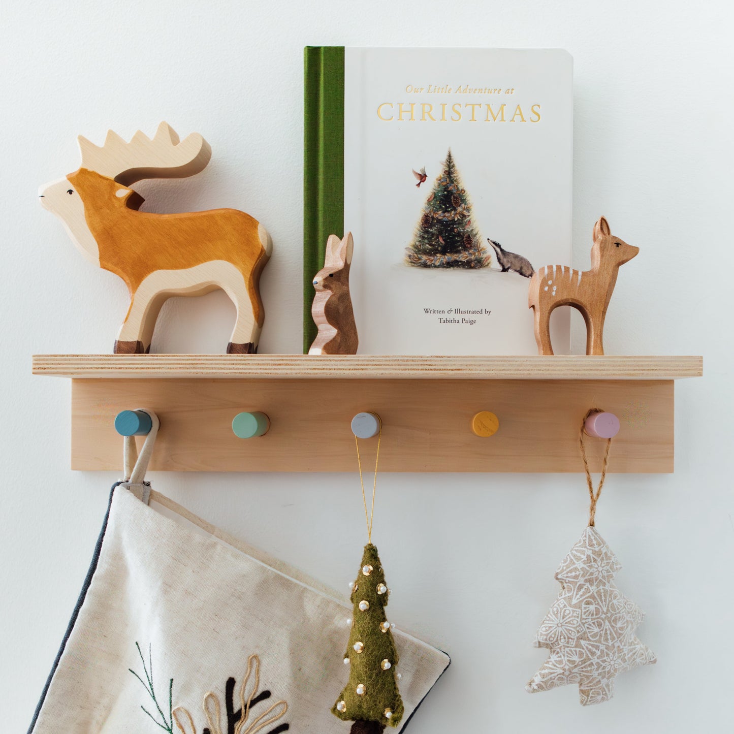 Wooden shelf with decorative items including a moose figurine, a book titled 'Our Little Adventure at Christmas', and small tree ornaments.
