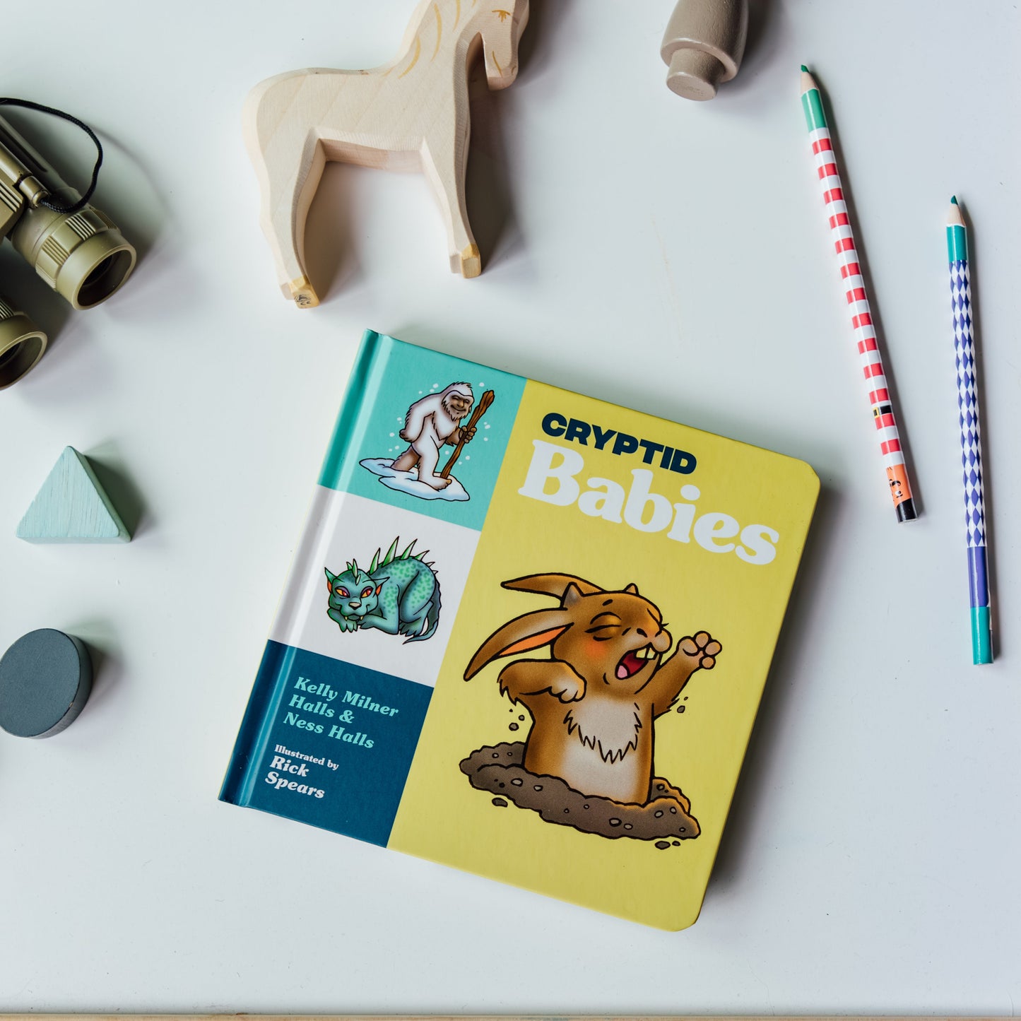 Book titled 'Cryptid Babies' on a table with toys and pencils around