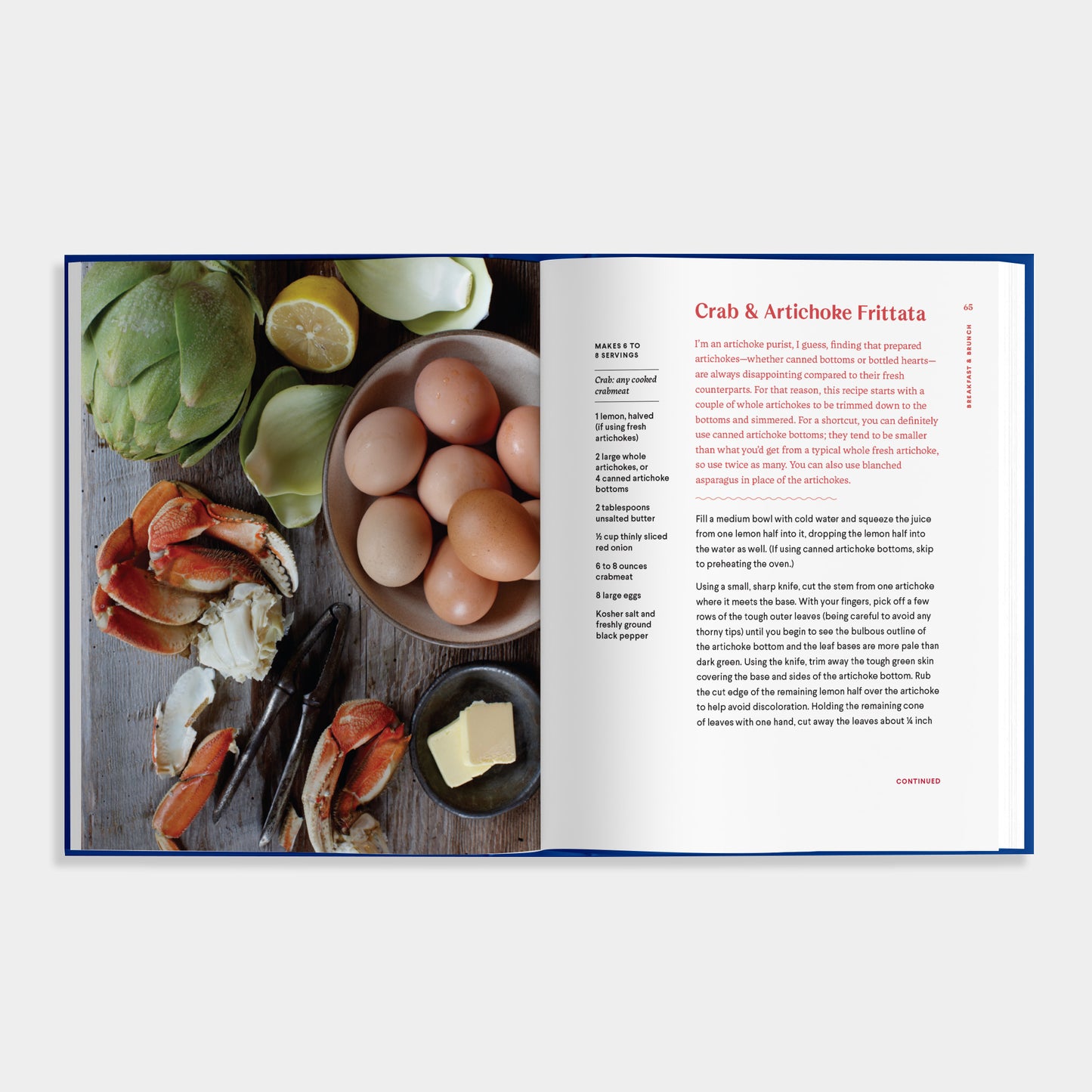 Open cookbook of Essential Shellfish Collection showing ingredients for Crab & Artichoke Frittata on a wooden board.