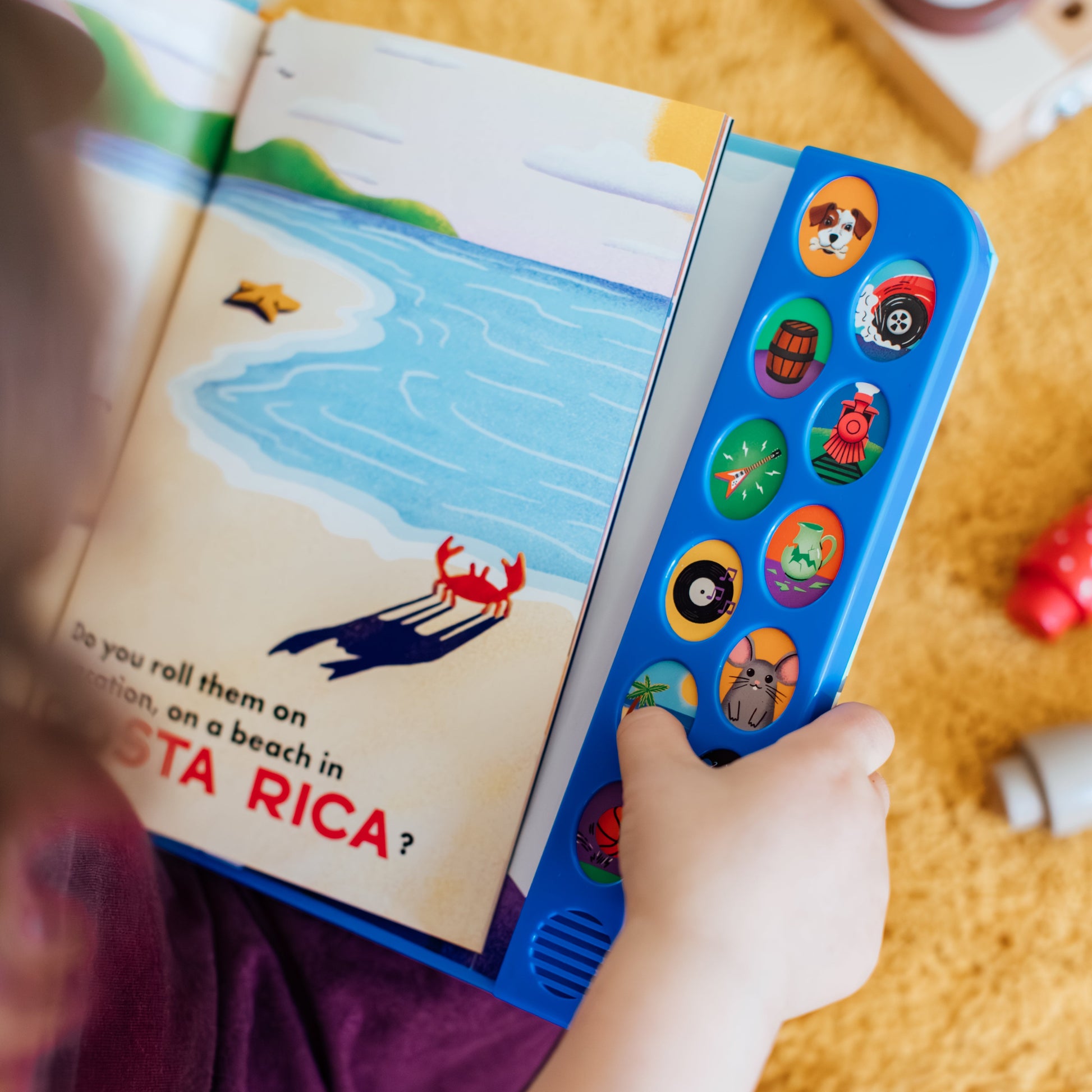 Child holding a "How Do You Roll Your R's" book and pusshing colorful buttons that make a sound on a yellow textured surface