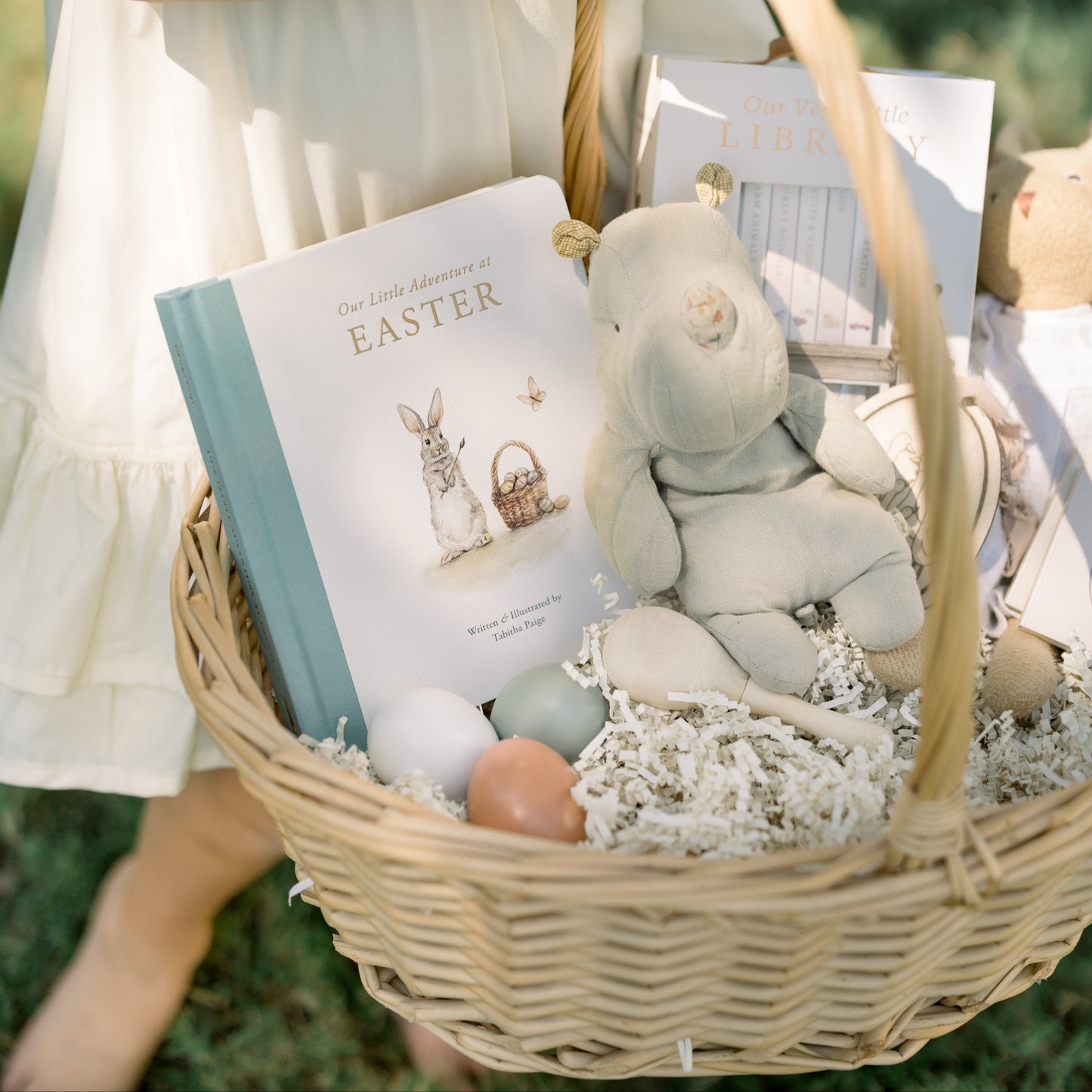 Child holding a Easter basket with a book and plush toy outdoors