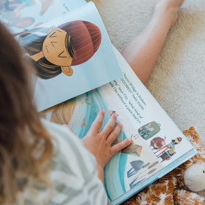 Child reading a children's book with a teddy bear on a carpeted floor