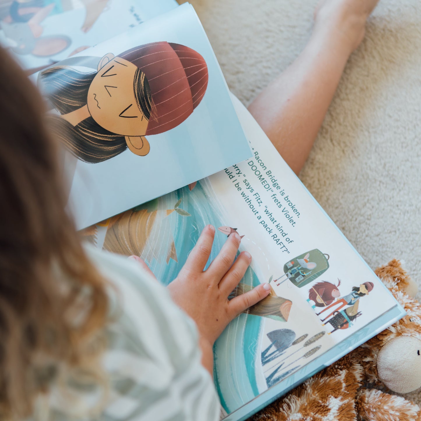 Child reading a children's book with a teddy bear on a carpeted floor
