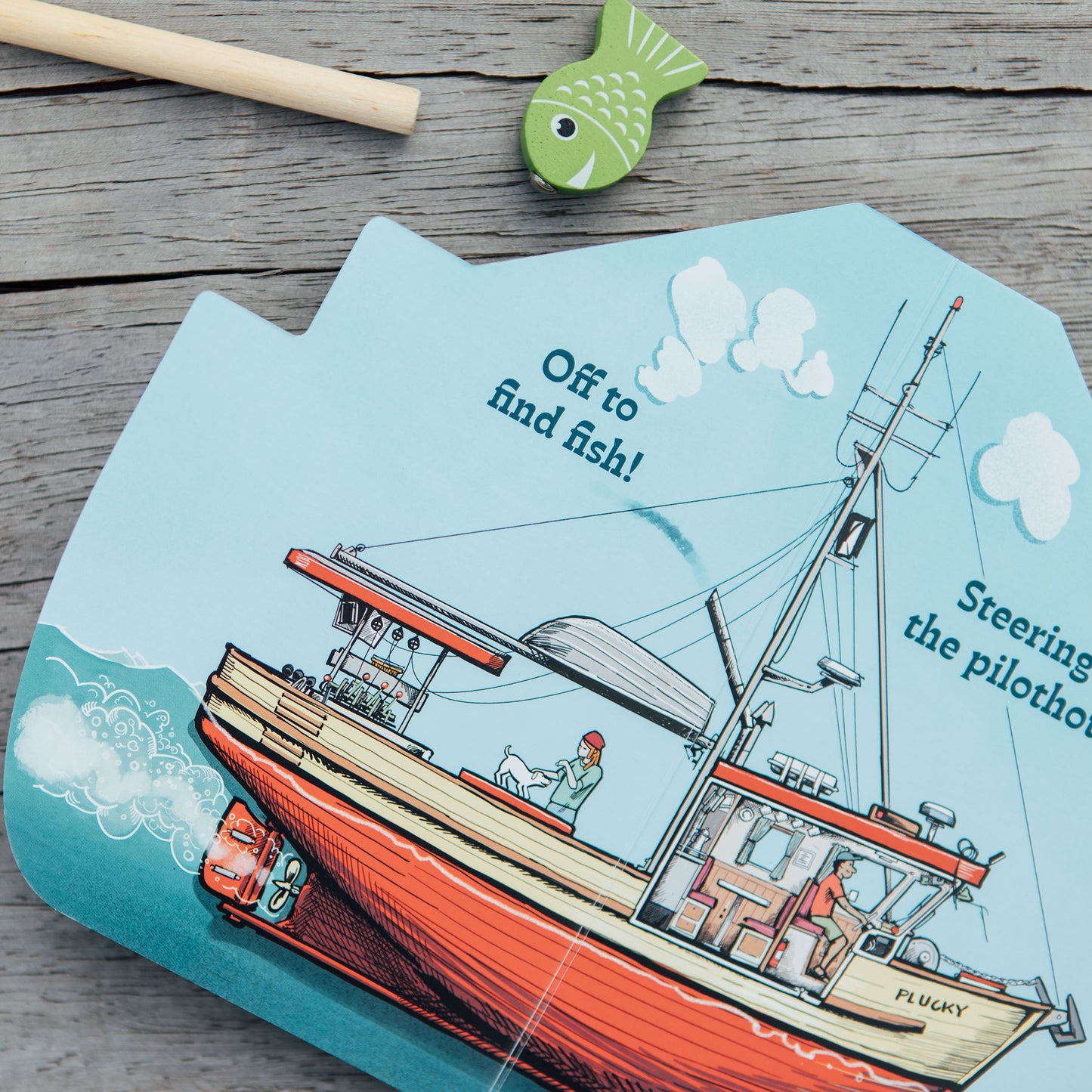 Children's book with a boat illustration on a wooden surface with toy fishing items.