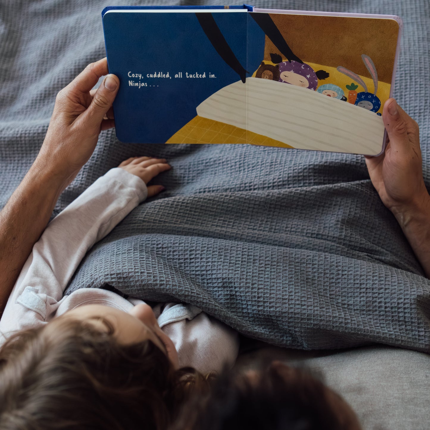 Person reading Good Night, Ninjas to a child on a bed