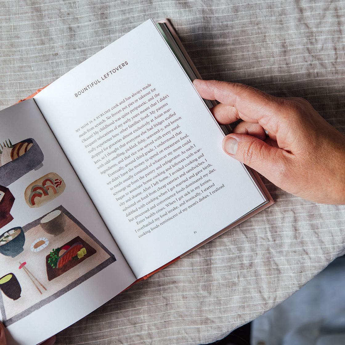 Person reading a book on a table with a teacup and teapot.