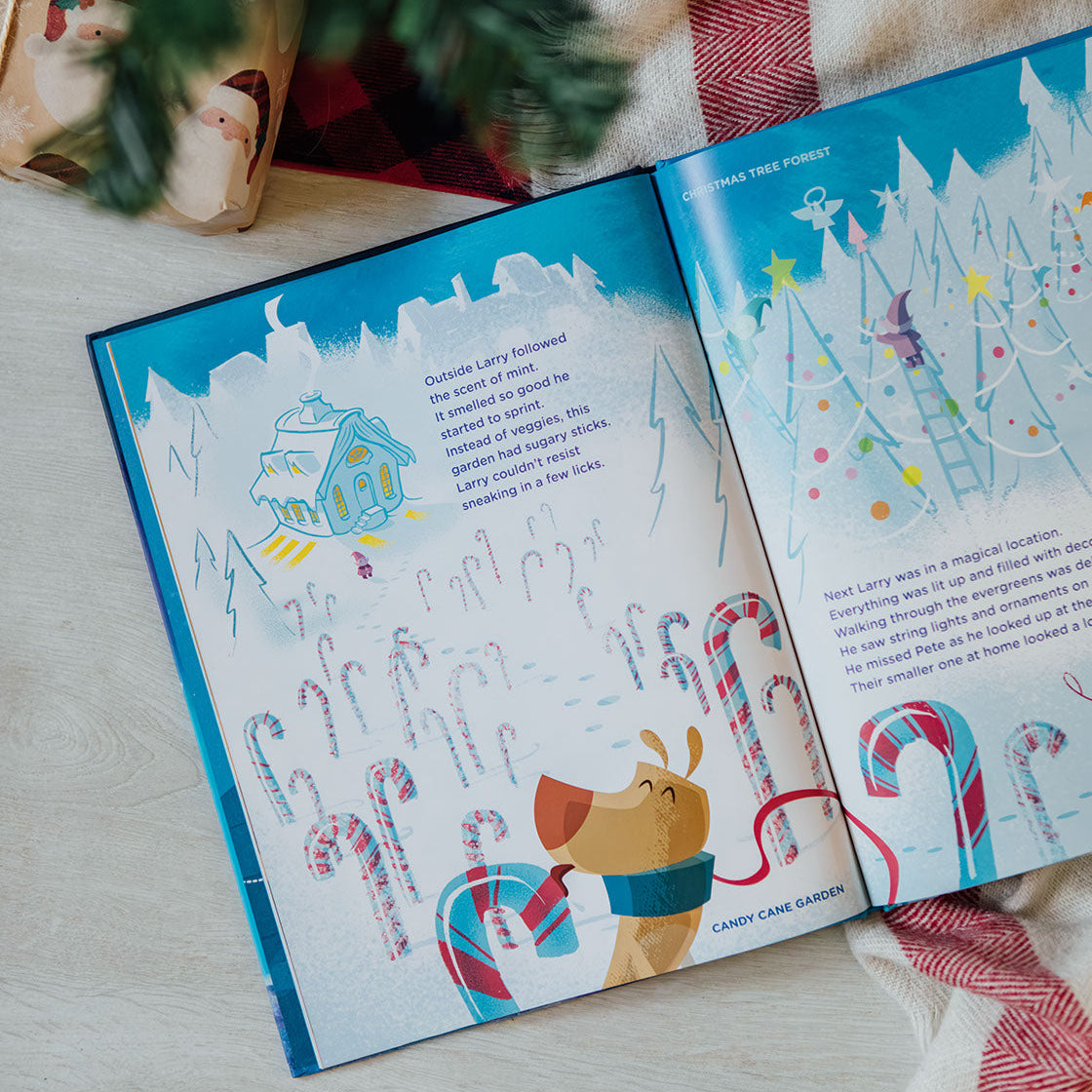 Open children's book with Christmas-themed illustrations on a wooden surface, surrounded by festive decor.
