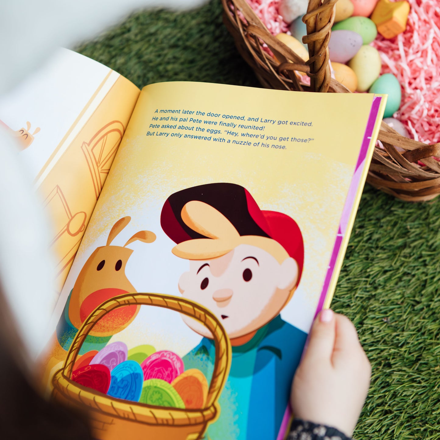 Child holding a colorful children's book with a character and Easter basket on a grassy surface.