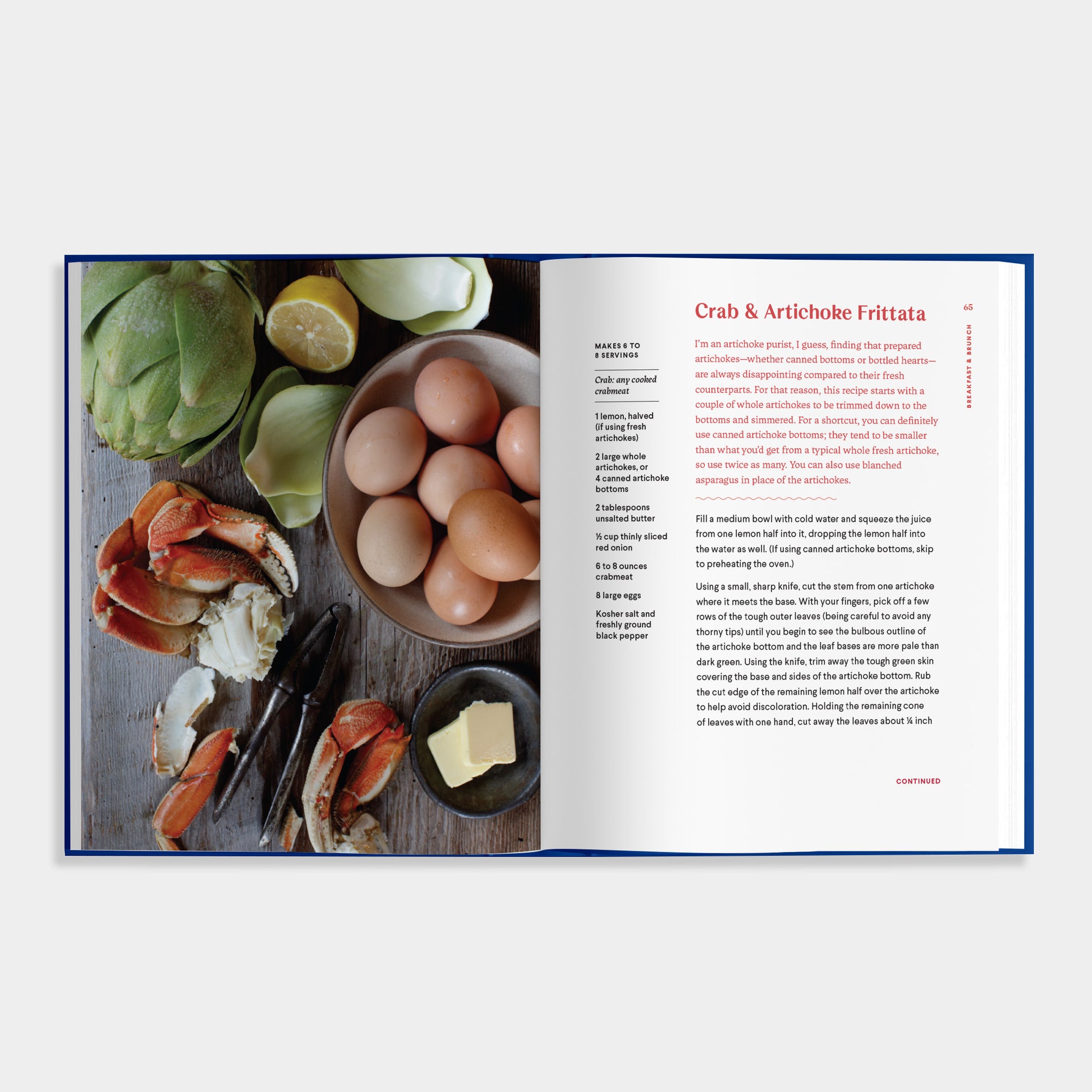 Open cookbook of Essential Shellfish Collection showing ingredients for Crab & Artichoke Frittata on a wooden board.