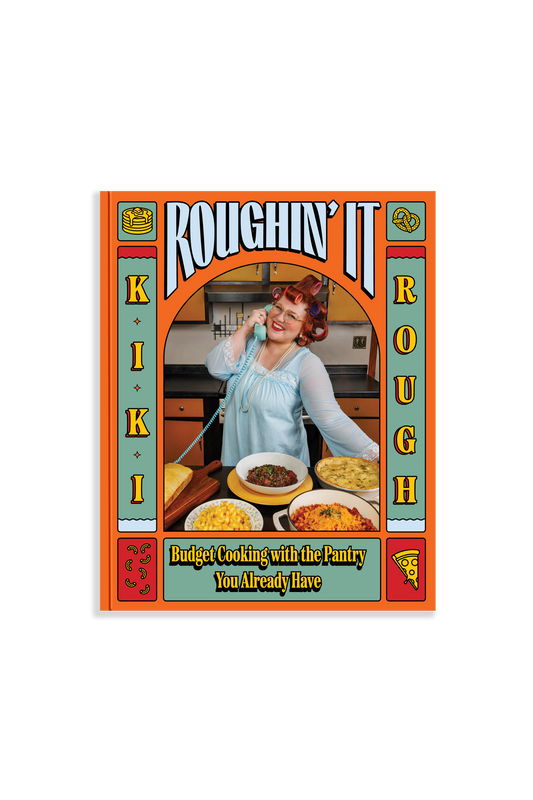 book cover of "Roughin' It" is orange an blue with a retro-style image of the author in a kitchen with a landline phone in her hand and several dishes of food on a table in front of her. 