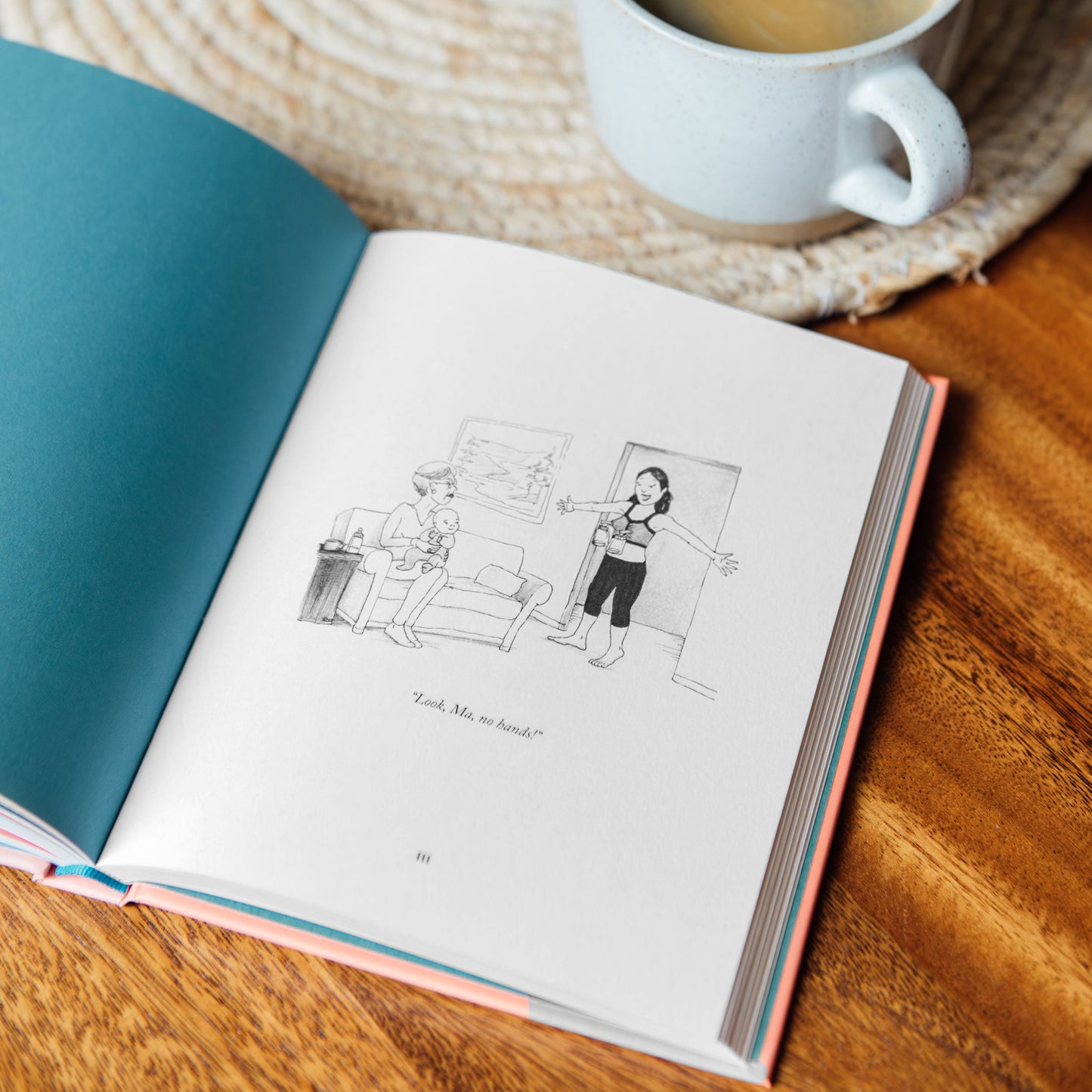 Open book with illustrations on a wooden surface next to a cup of tea and a plant.