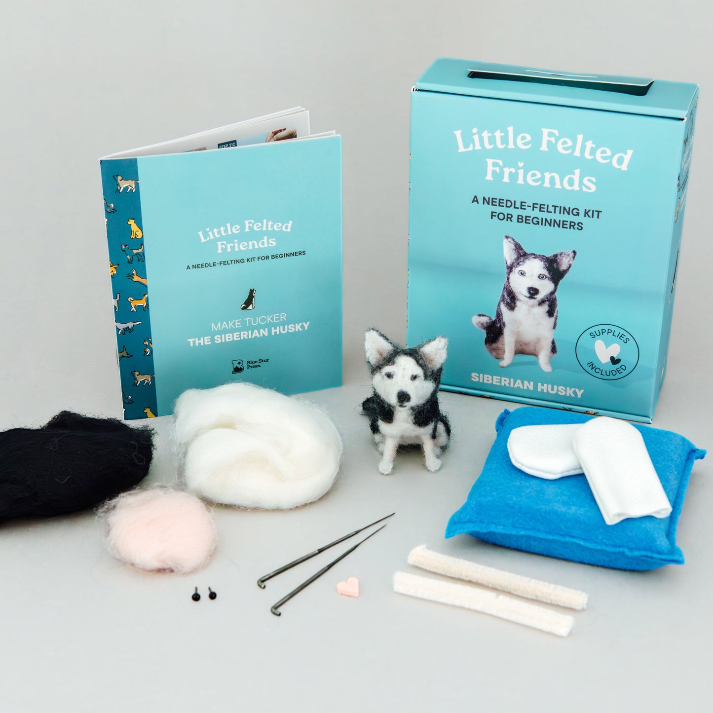 Needle felting kit with books, wool, and tools on a gray background