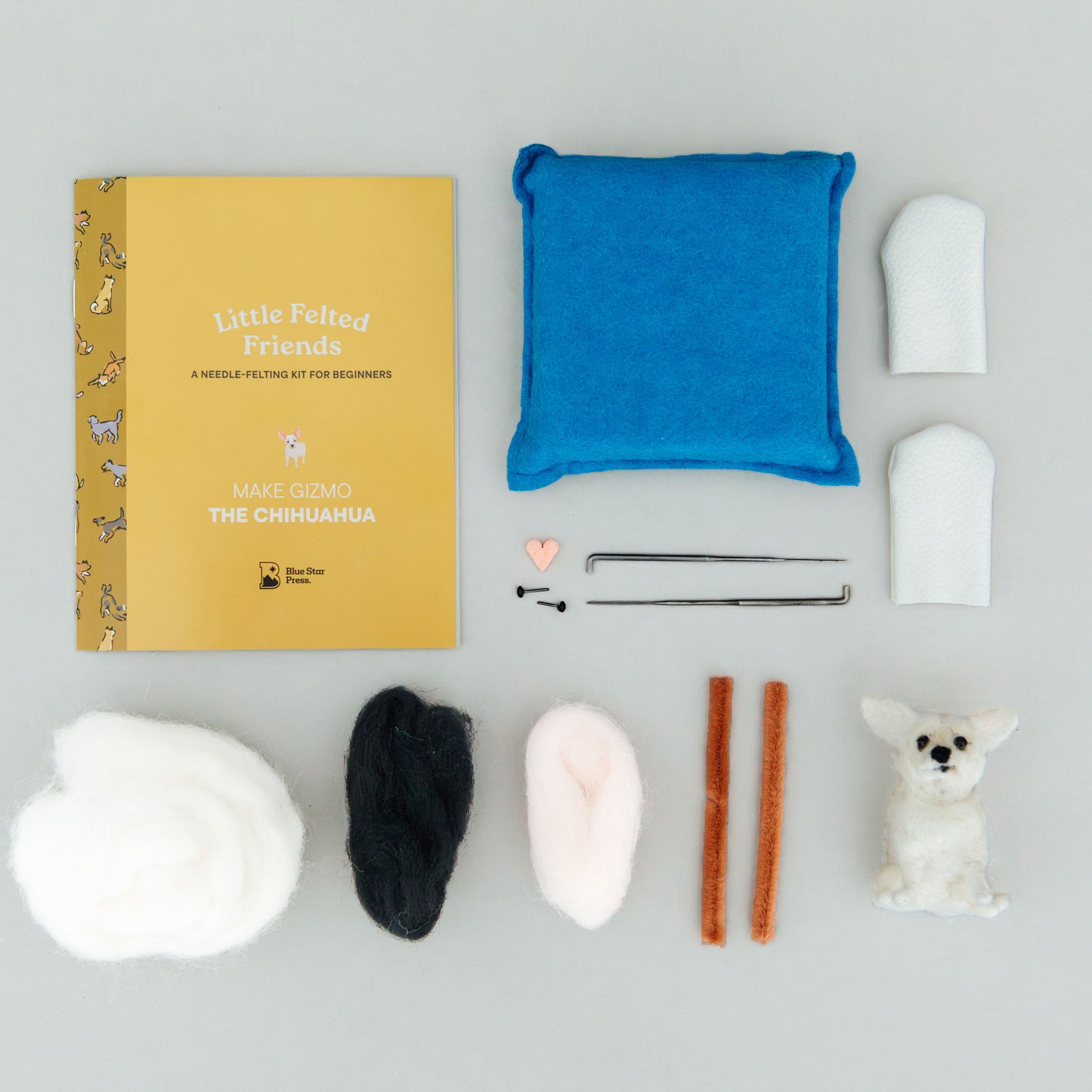 Collection of craft materials including a book, fabric pieces, and small figures on a gray background