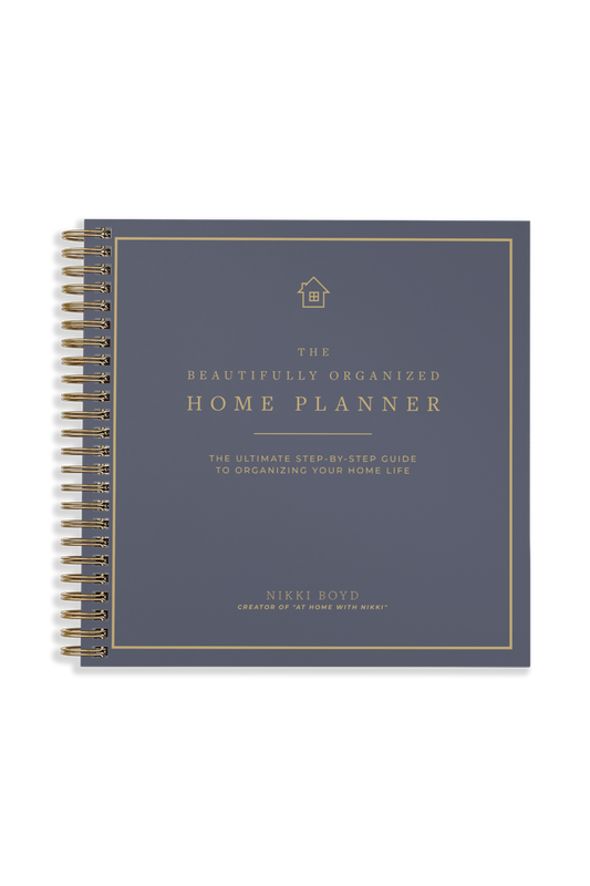 A spiral-bound home planner with a slate blue-gray cover and gold text and border details, shown on a plain white background.